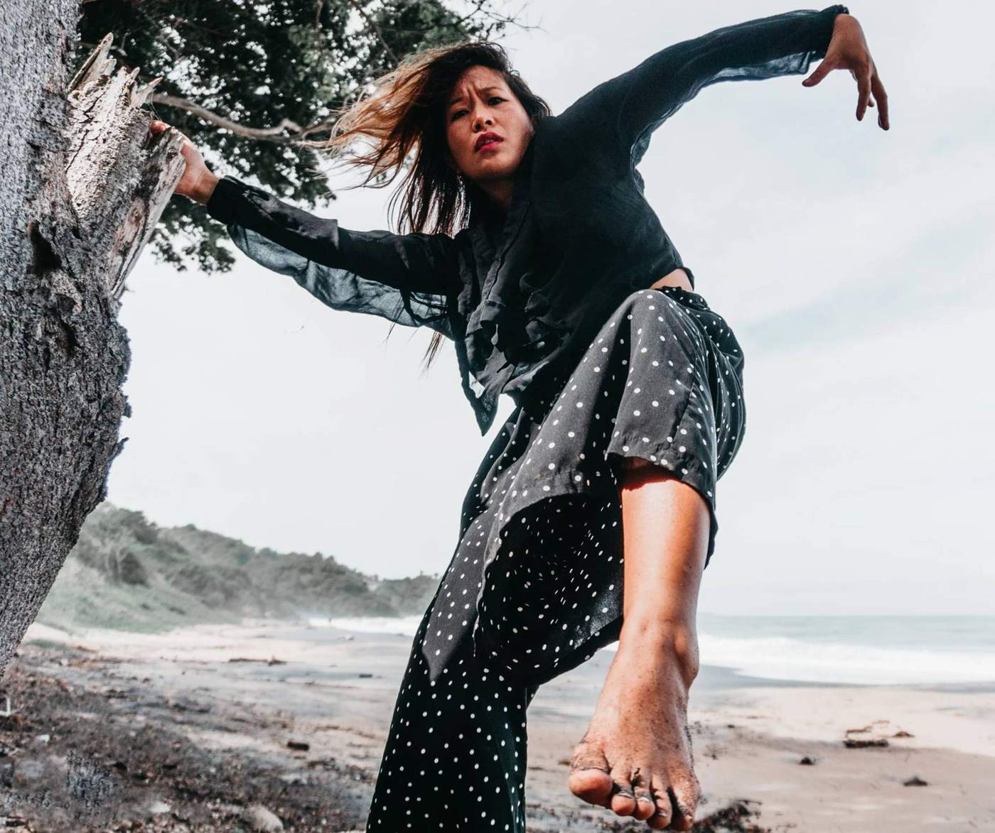A dancer moving barefoot on a beach by dark rocks