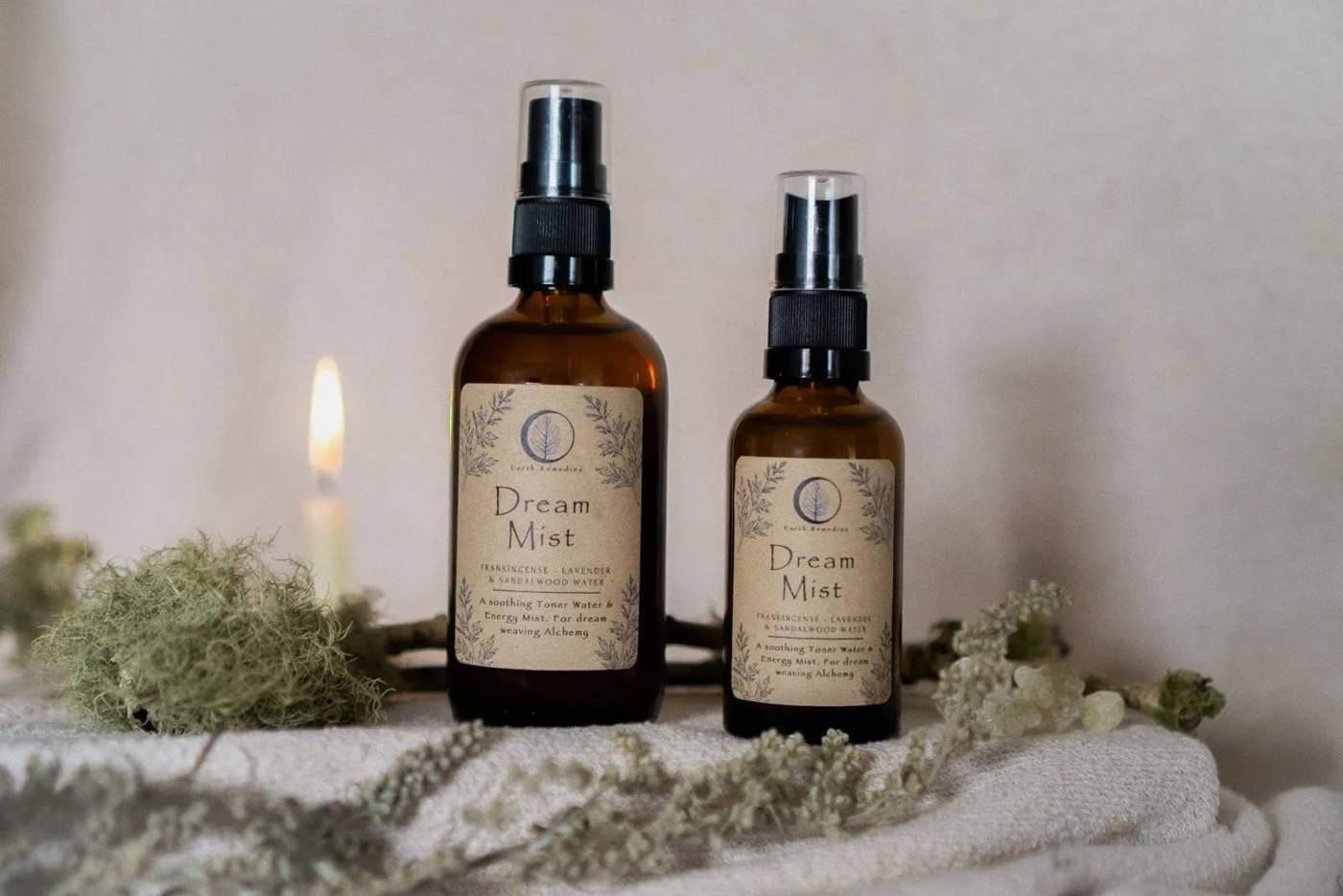 Two bottles of Dream Mist among moss and linen, with a lit candle